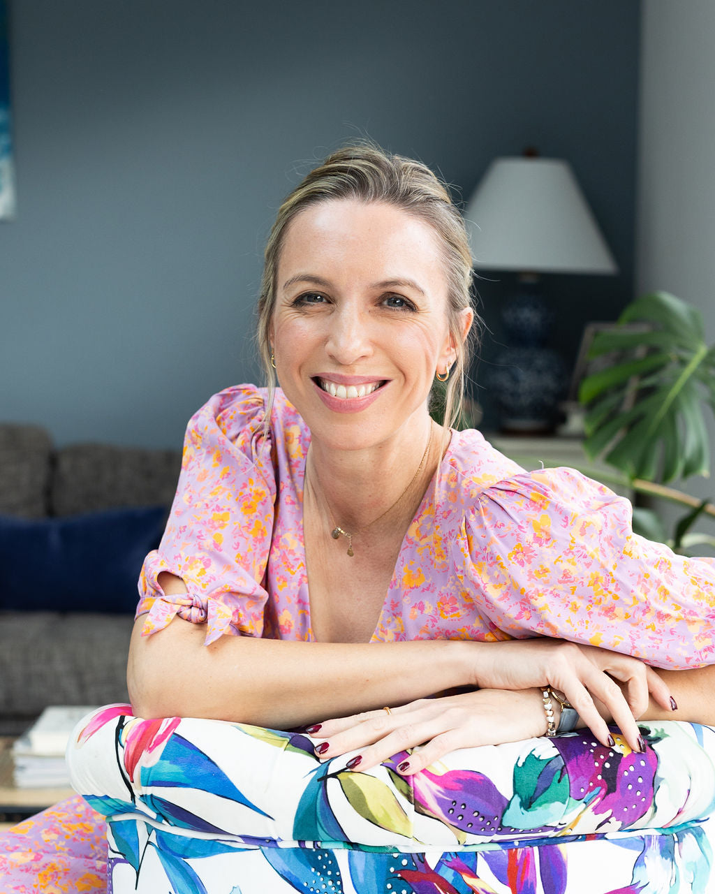A photo of Dr Emmie - a woman in a colorful outfit sitting on a couch in a living room.