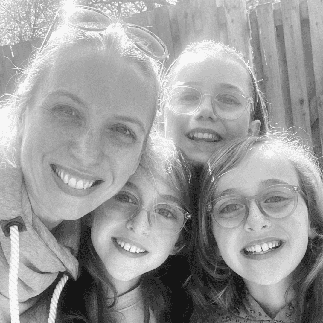 Black and white photo of Dr Emmie and her three young daughters smiling outdoors.
