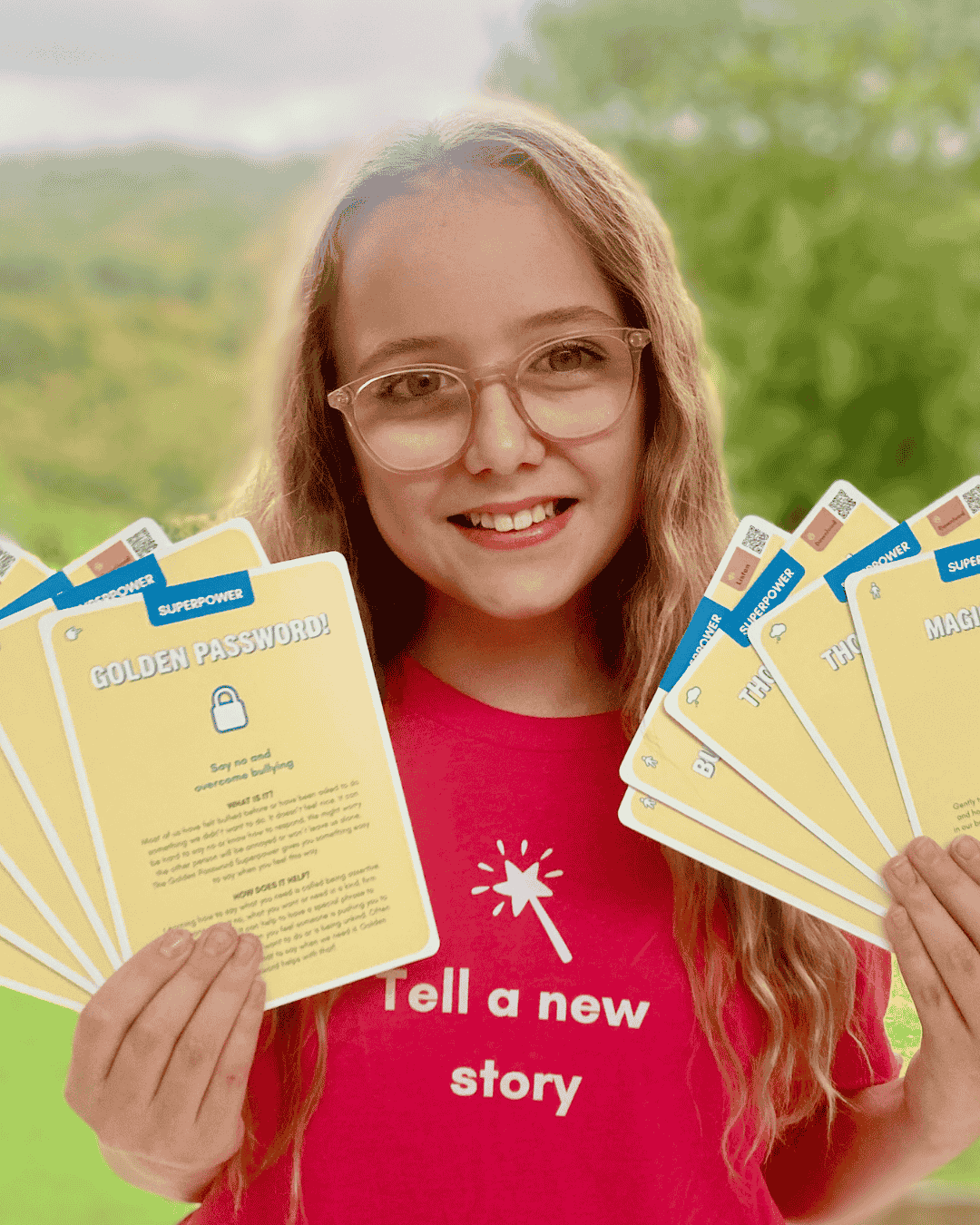 Girl in a red T-shirt holding several Superpower Cards with trees in the background