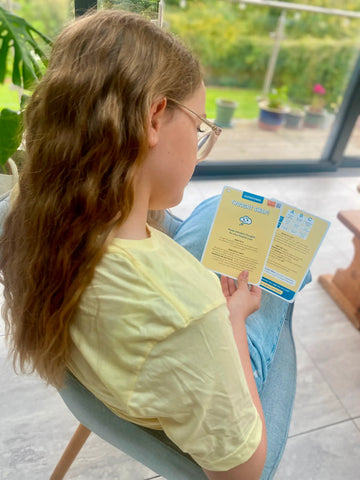 Person sitting on a chair holding a yellow superpower card with a garden view outside