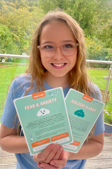 Older girl holding two Emotion cards about fear and anxiety and jealousy and envy.