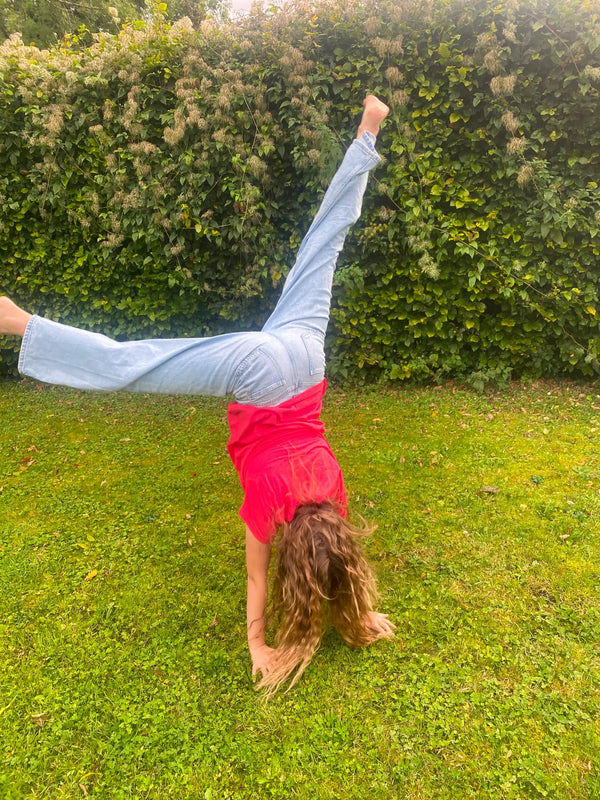 Girl doing a handstand on grass with a green bush background