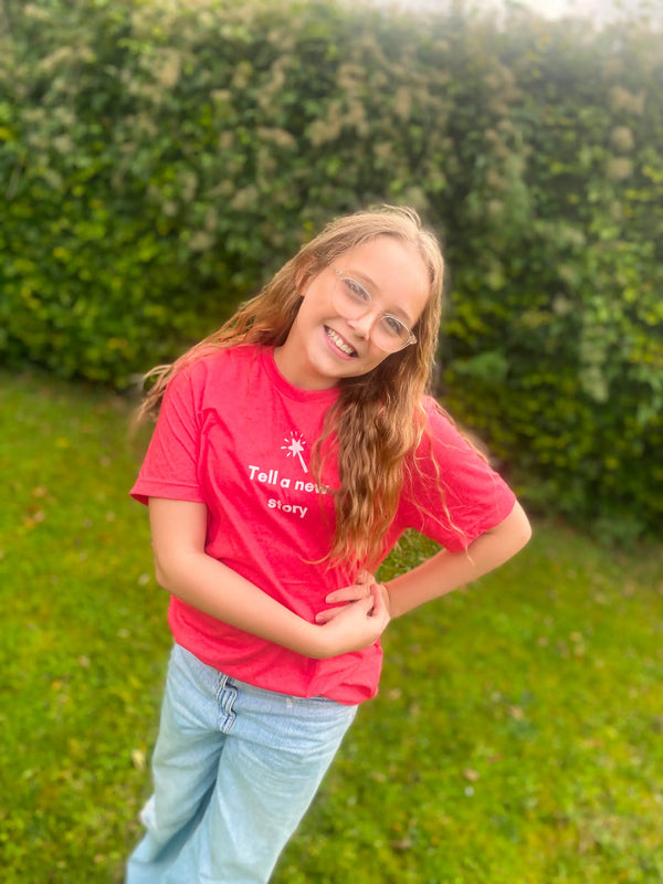 Young girl in a red shirt standing outdoors with greenery in the background